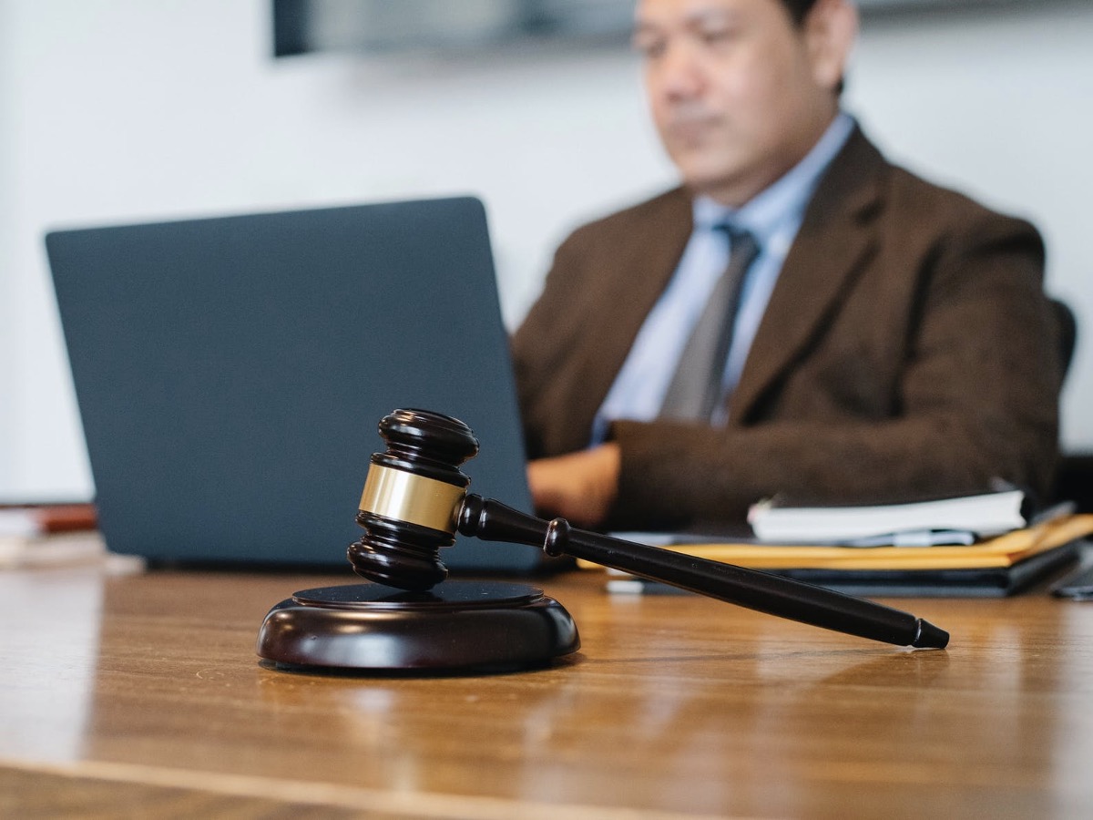 A man sitting with his laptop and a gavel in a courtroom
